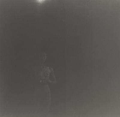 very dark black and white image of a nude woman holding a camera in front of her belly; received in silver frame